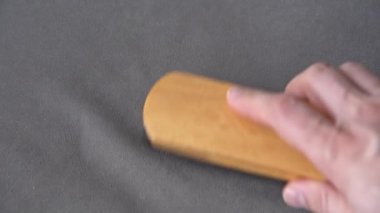 Kısa lifli gri kumaş serildi. Tahta temizleme fırçasını tutan bir insan elinin yakın çekimi. Bir insan gri kumaşı uzun bir fırçayla temizler..