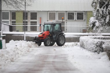 Kırmızı bir araç binaların önündeki karları temizliyor. Bloğun önündeki otoparktan taze kar kaldırıyorum. Şehirde kış mevsimi. Yoğun kar yağışı araba sürmeyi zorlaştırır..