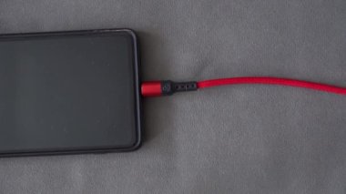 Adamın biri cep telefonu prizinin fişini çekiyor. Etkisiz hale getirilmiş bir cep telefonu masanın üzerinde duruyor. Cep telefonunun ve şarj aletinin fişini çeken adamın elleri..