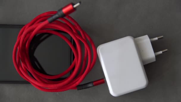 一只人类的手伸向一个白色充电器 它连接着一根红色盘绕的电缆 充电器和电缆放在手机的顶部 人类的手拿起充电器和电缆拿走了 那你的手 — 图库视频影像