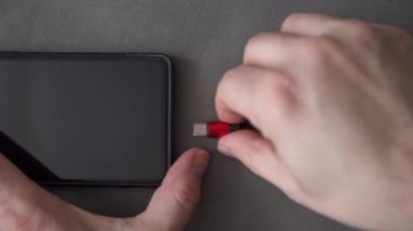 Mikro usb prizini telefon prizine bağlayan ellerin yakın çekimi. Cep telefonunu şarja bağlıyorum. Telefonlar şarj seviyesini gösteriyor..