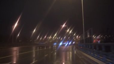 Araba asfalt bir yol boyunca ses engellerini aşarak ilerliyor. Kötü hava koşulları ve araba sürerken görüş mesafesi kötü. Bir yolcu vagonunun ön camından bak..