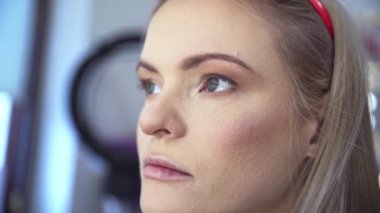 Güzellik salonunun hizmetinden yararlanan sarışın bir kadının yüzüne yakın çekim. Makyöz kaş makyajı yapıyor. Müşterilerin kaşlarına jel sürerek düzeltiyor. Bir kadınla.