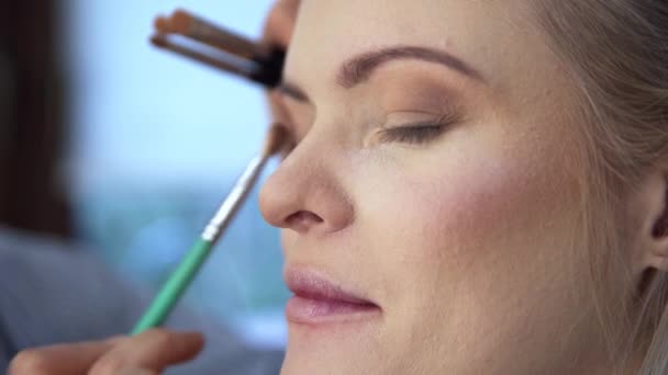 化妆师在眉线以下涂眼影 这个女人在美容院里 利用专业人士的服务 在棕色和米黄色的阴影中使用发光化妆品 — 图库视频影像