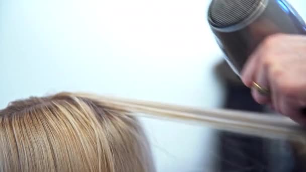 髪の長い金髪の女の頭の上のクローズアップ 女性は美容院のサービスを利用しています 美容師は丸いブラシとブロー乾燥に髪の鎖を巻き — ストック動画