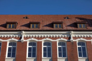 Perde duvarının ve çatının ön görüntüsü. Kırmızı tuğla ve kırmızı fayanstan yapılmış tüm bina. Açık mavi gökyüzü.