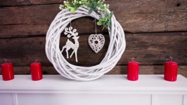 Hasırdan örülmüş dört kırmızı mum ve bir çelenk beyaz bir şöminenin üzerinde duruyor. Noel için mütevazı bir süs. .