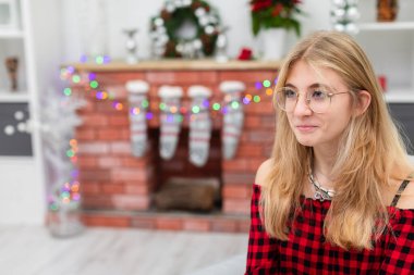 Genç kızın büstünü tuğla şöminenin arka planına yakın çekim. Kızın sarı saçları var. Tuğla şömine arka planda görülebilir. Bulanık ikinci plan.