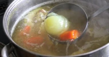 Close-up of the pot with which the broth is boiling. Dipping a tureen spoon into the broth and stirring several times. Removing onions and other vegetables from the broth to the surface.
