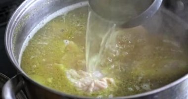 Çorbanın kaynadığı tencereye yakın çekim. Çorbaya bir kaşık batırıp birkaç kez karıştırmak. Yağlı bir tavuk ve havucu et suyundan yüzeye çıkarmak..