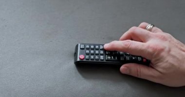 TV uzaktan kumandası bir erkek tarafından kullanılır. Adamın eli işaret parmağıyla TV kanallarını değiştirmek için düğmeye basıyor..