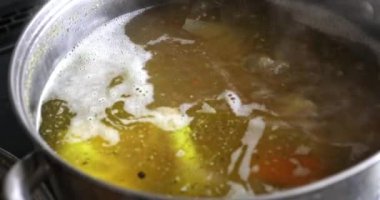 Kaynayan çorbanın yüzeyine yakın çekim. Yukarıdan görünen bir tencere çorba. Et suyu kaynıyor ve yüzeyi titriyor. Çorbanın yüzeyinde yemek pişirme nedeniyle köpük oluştu..