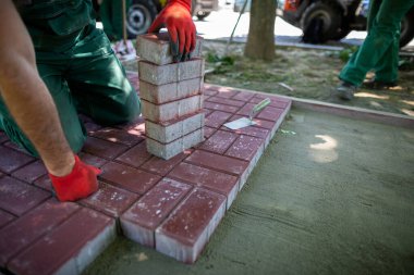 Asfalt döşeme çalışmaları sırasında, çalışan her beton bloğu yerleştirirken doğruluğu sağlamak için dikkatli davranır. Ağır ve zahmetli inşaat işi.