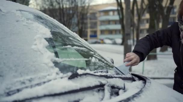 一个女人站在雪地上 一个女人站在她的车旁边 她正在从车上铲雪 这个女人用刮胡刀把汽车挡风玻璃上的雪和汽车上的雪都刮掉 — 图库视频影像