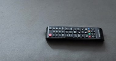 TV uzaktan kumandası yumuşak kanepede yatıyor. İşaret parmağıyla, adamın eli TV kumandasındaki ses yükseltme düğmesine basıyor..