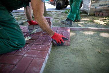 Kaldırımda döşeme yaparken elle kaldırım çalışması. Profesyonel bir asfalt döşeme müteahhidi kaldırımda dizlerinin üzerine çöküp dikkatlice çalışır..