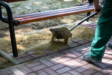 Bir işçi yeni bırakılmış kaldırım taşlarına kürekle kum taşır. Kaldırım döşemeden sonraki son adım kum ile oluşan boşlukları tıkamaktır..