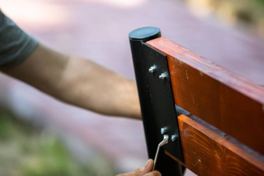 Bir inşaat işçisi yeni bir park bankında ahşap ve çelik parçaları birlikte büker. Yaz güneşi her yaz ışıldar..