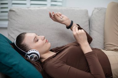 Kanepede yatan bir kızın kafasının yakın çekimi. Kızın kulaklığı kulağında ve müzik dinliyor. Kafasının altında turkuaz bir yastık var. Kız uzun kollu kahverengi bir şey giyiyor.