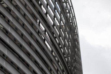 Spor salonunun tepesinin beyaz bulutlarla kaplanmış mavi gökyüzüne bakan görüntüsü. Metal panellerden yapılmış binanın modern cephesi.