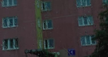 Yağan yağmur araba sürerken ön camı ıslatır. Islak ön camın arkasından park etmiş arabaları ve alçak bir binanın çatısını görebilirsin..