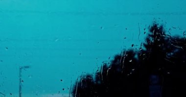 Dışarıda yağmur yağıyor çünkü bardaktaki su damlalarını ve damlalarını görebilirsiniz. Arka planda, bulanık ağaç şekilleri ve yüksek voltaj direklerinin ana hatları var..