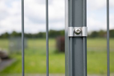 Çelik direğe düzgün yerleştirilmiş çit paneli. Bulanık gökyüzü ve yeşil çimlerle ikinci plan.