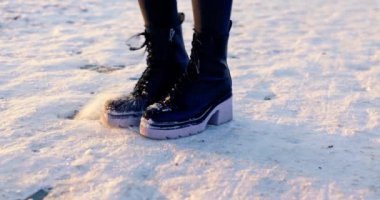 Bir kadının bacaklarının yakın çekimi. Kadın kalın tabanlı kışlık ayakkabılar giyiyor. O, karın üzerinde duruyor. Botlar karla kaplı. Kadın sürekli kardan kurtulmak için pul yapıştırıyor.