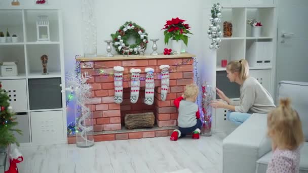 Kobieta Pokazuje Chłopcu Świąteczne Dekoracje Przy Kominku Cegły Pobliżu Stoi — Wideo stockowe