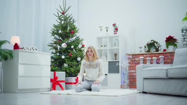 ある若い女性が息子を勇敢に引き上げ 彼女に駆けつけた 女性はクリスマスツリーから遠くない白いカーペットの上に座っています クリスマスツリーは休日の装飾で飾られています — ストック動画