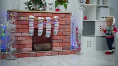 Odada bir çocuk dolaşıyor. Raflara bakıyor, tuğla şöminenin yanından geçiyor, Noel süslerine bakıyor ve onlara dokunuyor. Şöminenin önünde duruyor ve koşuyor..
