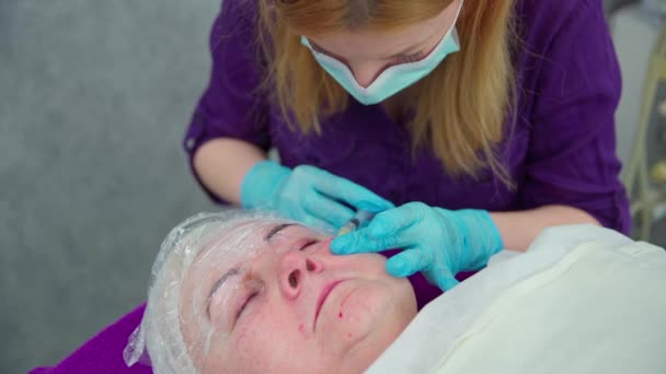 美容師はクライアントの肌の下で製品を注射する 高齢の女性がメセラピー治療を受けている美容院に横たわっています 新鮮な穿刺マークは女性の顔に表示されます — ストック動画