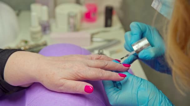 一个在美容院修指甲的成熟女人的手部特写 女人把她的手放在紫色的垫子上 造型师正在用一次性手套工作 — 图库视频影像