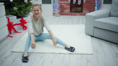 At kuyruğu taranmış bir kadın beyaz bir halıya oturur. Odada birçok Noel süsü, ışık ve altında hediyeler bulunan süslü bir Noel ağacı görebilirsiniz. Kadın gülümsüyor, etrafına bakıyor.