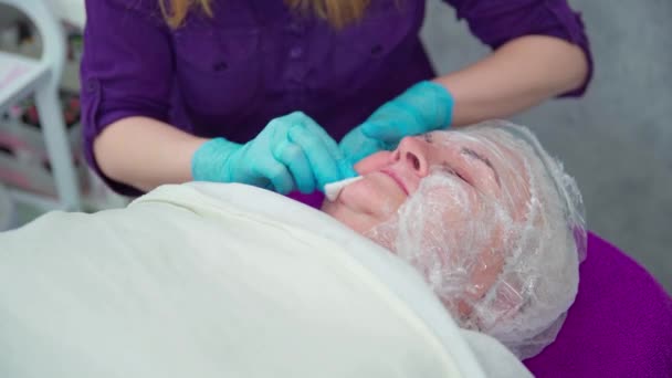 美容院的工作人员小心地用棉签擦拭顾客的脸 那位美容师穿着紫色的制服 沙龙的顾客是个老太婆 — 图库视频影像