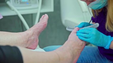 Kozmetik uzmanı tek kullanımlık nitril eldivenlerle çalışıyor. Uzman cerrahi maske ve mor iş üniforması giyiyor..