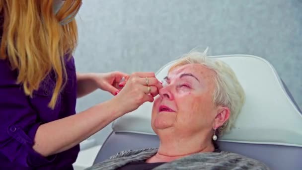 美容院的顾客有一双红眼睛 美容师用浸有盐水的棉签擦拭妇女的眼睛 女人眨眼很快 她的眼睑是红色的 — 图库视频影像