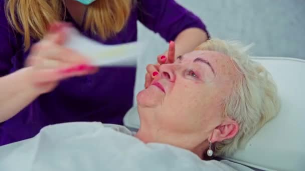 一个女人躺在美容院的一张化妆品床上 美容师多次在客户的鼻子下面贴上并剥下一片白色的脱毛蜡 摘除面部毛发 — 图库视频影像