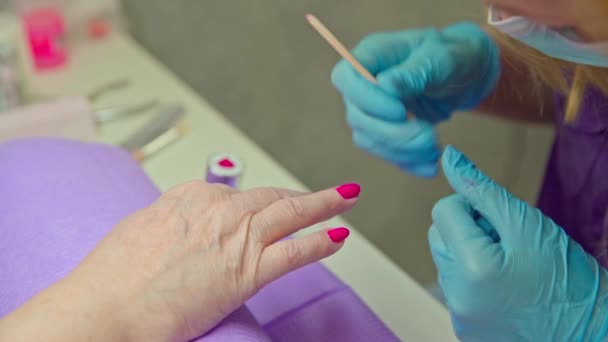 一个在美容院工作的女孩用混合指甲油进行指甲绘画服务 在顾客的密切合作下 她的指甲漆成了粉红色 — 图库视频影像