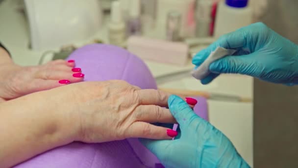 一个成熟女人的手的特写 她把双手放在紫色的枕头上 对面坐着一位美容师 她用浸透了清洁剂的棉签擦拭顾客的指甲 — 图库视频影像