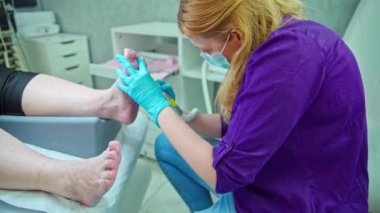 Pedikür yapan bir güzellik uzmanı müşterisinin ayaklarının üzerine eğilir. Pedikür deneyimi yaşayan kadın kozmetik yatağında yatıyor, sadece ayakları görünüyor..