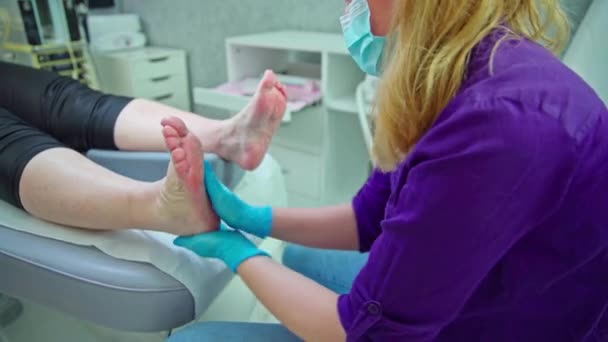 化粧品店で働く女性は クライアントの足の世話をします 女性は化粧台の上に横たわっている 足と足だけが見えています 美容師は彼女の足にスクラブを適用する — ストック動画