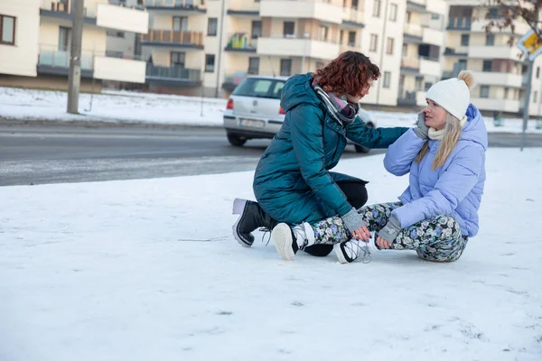A kind-hearted woman helps a person who is sitting in the snow. The girl slipped and fell. The young person needs medical attention.