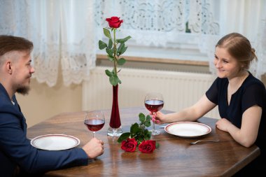 Birbirine aşık bir çift masada oturur ve birbirlerinin gözlerinin içine bakar. Masanın üzerinde kırmızı gül, tabak ve iki kadeh kırmızı şarap olan bir vazo var.