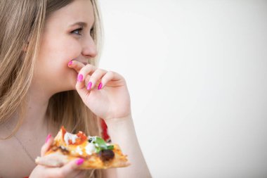 Mutlu genç bir kadının profil görüşü. O gülüyor ve eliyle ağzını örtüyor. Diğer elinde ise bir dilim pizza tutuyor. Dilim kemirilmiş..