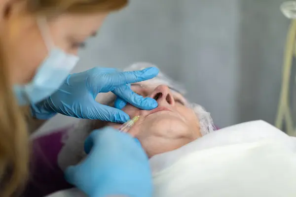 A patient at an aesthetic medicine clinic is experiencing painful injections around her mouth. A cosmetologist makes punctures with a thin needle and injects the product subcutaneously.
