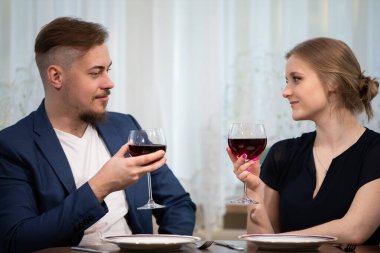 Bir erkek ve bir kadın karşılıklı oturup birbirlerinin gözlerinin içine bakarlar. İkisi de şık kıyafetler giyiyor. Kadehlerini kırmızı şarapla kaldırırlar ve kadeh kaldırırlar..