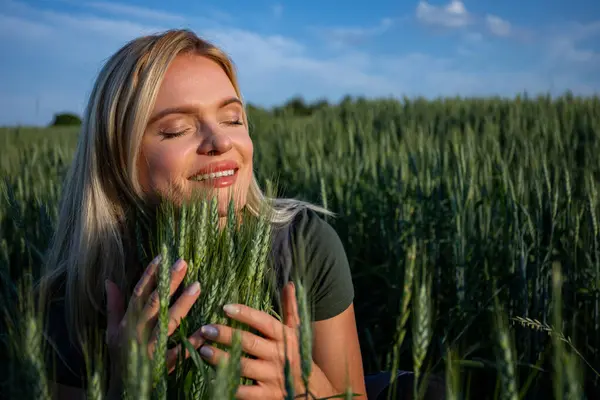 stock image In the heart of the field, a smiling female farmer affectionately embraces towering ears of grain. Her radiant smile reveals her teeth as she lovingly cradles the lush wheat with both hands. With