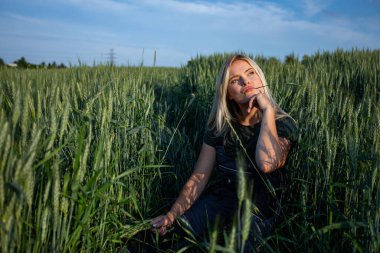 Kırsal bir buğday tarlasının huzurlu boşluğunda dişi bir çiftçi bir elinde buğday sapı tutarak dudaklarının yakınına yerleştiriyor. Güneş yanığı teniyle ve iş kıyafetleriyle...
