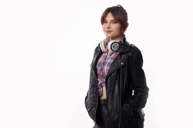 Moda ve modaya uygun genç bir kadın kendine güvenerek poz veriyor, şık bir deri ceket ve moda kulaklıklar takıyor.